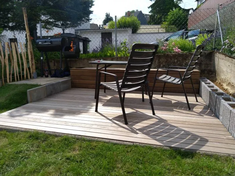Kleine Holzterrasse im Garten mit Tisch und Stühlen auf dem Rasen